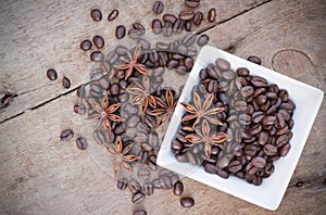 Coffee beans and star anise in a white bowl on wooden background