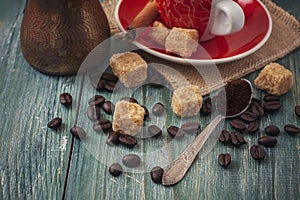 Coffee beans, sugar and red cup of coffee on wooden background.