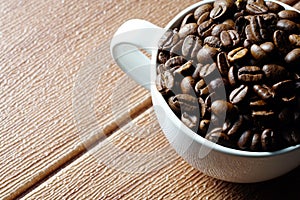 Coffee beans in a white cup over the wooden surface