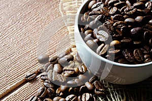 Coffee beans in a white cup over the wooden surface