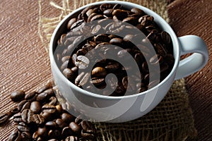 Coffee beans in a white cup over the wooden surface