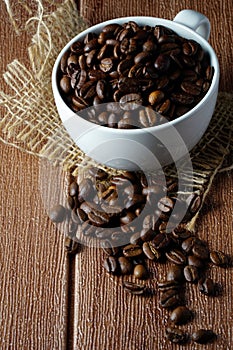 Coffee beans in a white cup over the wooden surface