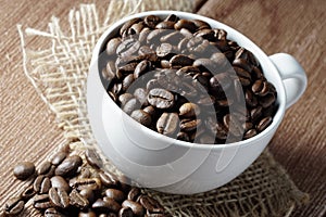 Coffee beans in a white cup over the wooden surface