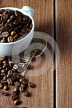 Coffee beans in a white cup over the wooden surface