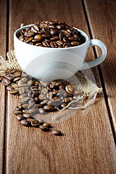 Coffee beans in a white cup over the wooden surface