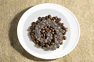 Coffee beans on white saucer. sackcloth background