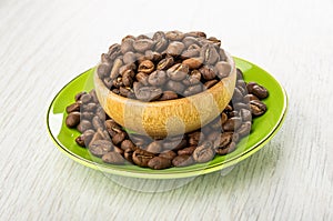Coffee beans in wooden bowl and in green saucer on light table