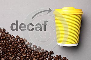 Coffee beans, word Decaf and arrow pointing at takeaway paper cup on light grey background, flat lay