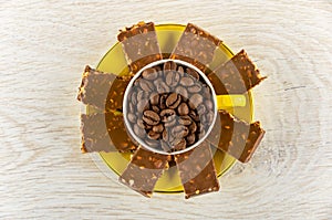 Coffee beans in yellow cup, pieces of chocolate on saucer on table. Top view