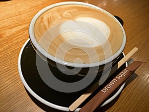Coffee in black cup. Heart latte art. Brown sugar.