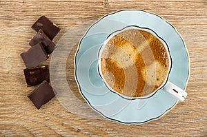 Coffee in blue cup on saucer, dark chocolate on table. Top view