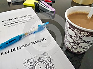 coffee, blue pen, and a book with DECISION MAKING written on it and an explanation in Indonesian.