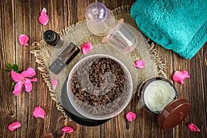 Coffee body scrub, sugar and coconut oil, essential oils, massage vacuum jars on dark wooden rustic table with pink flowers