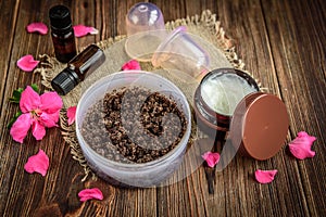 Coffee body scrub, sugar and coconut oil, essential oils, massage vacuum jars on dark wooden rustic table with pink flowers