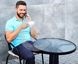 Coffee break brings physical and mental wellbeing. Man sit terrace and drink cappuccino speak phone grey wall background