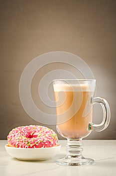 Coffee break: cappuccino glass with fresh sugary pink donut/Coffee break: cappuccino glass with fresh sugary pink donut on a gray