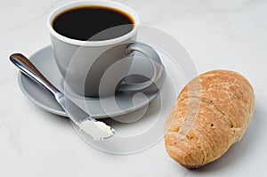 Coffee break with croissant, butter knife and cup of black coffee on a white stone table
