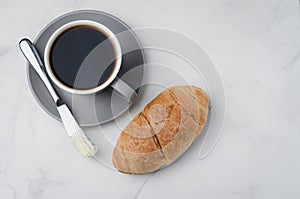Coffee break with croissant butter knife and cup of black coffee on a white stone table. Top view and copyspace