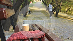 Coffee break on empty bench in autumn city park, blurred teenage male at public park walkway on background