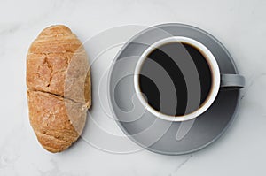 Coffee break. Grey cup with black coffee and croissant on white stone background. Top view