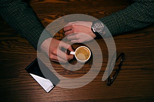 Coffee break. Man hand keep a cup of coffee on a wooden table. Phone and glasses. Business situation.