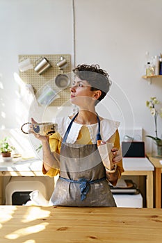 Coffee break in studio: woman potter drink tea from handicraft mug in creative ceramic art workshop