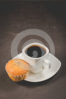Coffee break. White cup of the hot black coffee and muffin, top view, selective focus. Breakfast concept