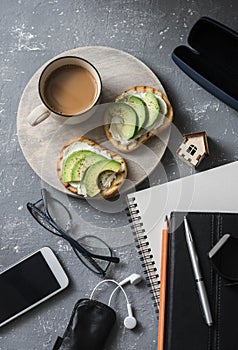 Coffee break during working hours. Flat lay business workplace with notebook, tablet, phone, glasses. Coffee and sandwich with cre