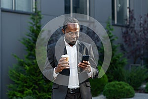 Coffee break. A young African-American businessman near the office. He holds a coffee and phone