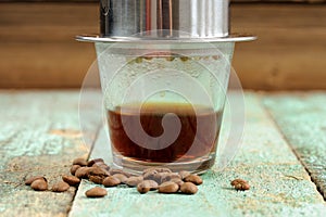 Coffee brewed in small metal French drip filter on wooden table