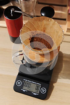 Coffee brewing in glass pour over with paper filter. Electronic scale, red manual grinder