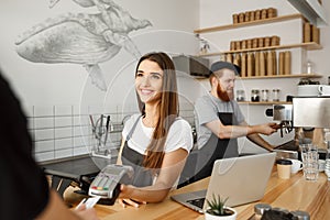 Coffee business concept - beautiful female barista giving payment service for customer with credit card and smiling