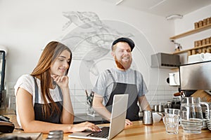 Coffee business concept - happy young couple business owners of small coffee shop working and planing on laptop.