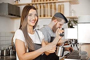 Coffee Business Concept - portrait of lady barista in apron preparing and steaming milk for coffee order with her