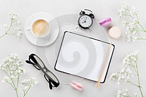 Coffee, cake macaron, notebook, eyeglasses, alarm clock and flower for breakfast on table top view. Woman working desk. Flat lay.