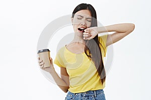 Only coffee can fight sleep. Tired and sleepy cute female coworker in yellow t-shirt yawning with closed eyes covering