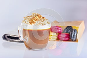 Coffee, cappuccino in a glass mug with whipped cream and ground nut. Macaron cakes in a paper bag, newspaper.