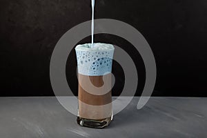 Coffee Cappuccino or latte with blue foam. Almond milk with blue matcha is poured into tall glass. Selective focus  dark