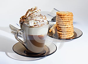 Coffee, cappuccino with whipped cream sprinkled with chocolate chips, ground nuts, cinnamon. Oatmeal cookies, stacked on a plate.