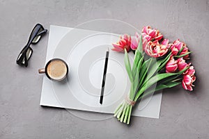 Coffee, clean notebook, eyeglasses and beautiful flower on stone table top view in flat lay style. Woman working desk.