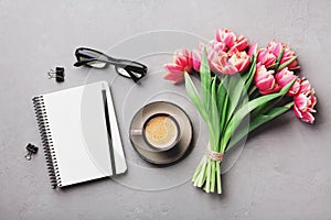 Coffee, clean notebook, eyeglasses and beautiful tulip flower on stone table top view in flat lay style. Woman working desk.