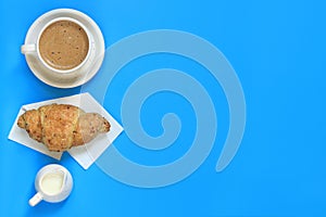 Coffee and croissant on a blue background. Flat lay, top view. Copy space