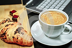 Coffee, croissant and laptop on the table. Business breakfast concept
