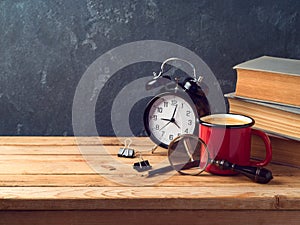 Coffee cup, alarm clock and old books on vintage wooden table