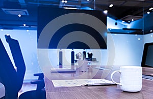 Coffee cup ,ballpoint pen and paperwork on table with blank screen television background in meeting room