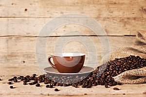 Coffee cup, beans and a burlap bag on old wooden background