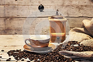 Coffee cup, beans and grinder in front of vintage wooden backgr