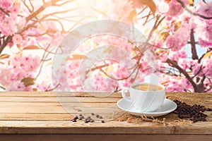Coffee cup with coffee beans on wooden table over blossom cherry tree blurred background with copy space