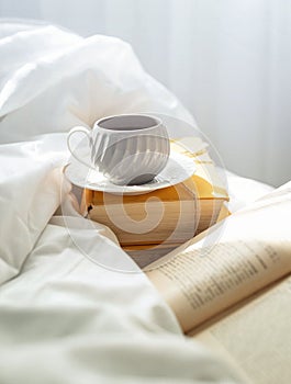 coffee cup and book sitting on the edge of a bed