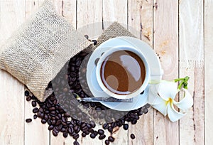 Coffee cup with burlap sack of coffee beans on wooden table